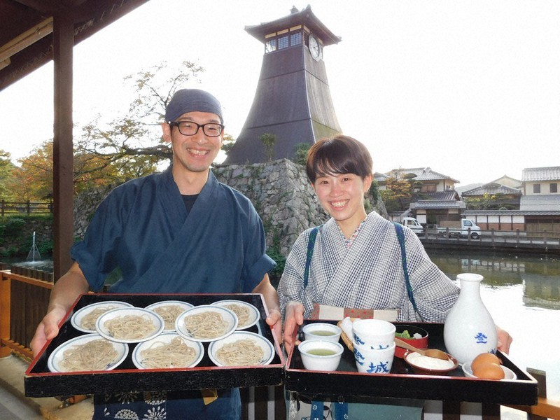 辰鼓楼の前の堀に面したテラス席で、自慢の皿そばPRする「登城」店主の竹中光成さん(左)と妻沙耶香さん=豊岡市出石町八木で2020年10月20日午後3時55分、村瀬達男撮影