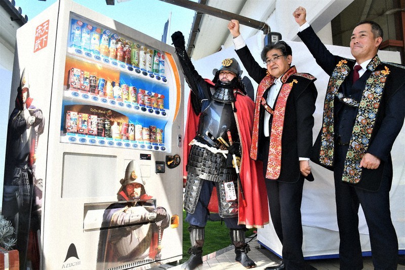 「織田信長自動販売機」を前に、安土の観光促進へ向け気勢を上げる小西理・近江八幡市長(中央)ら=滋賀県近江八幡市安土町小中の安土城郭資料館前で、礒野健一撮影
