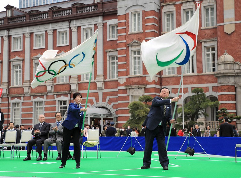 全国を巡回し東京に戻ってきた五輪旗とパラリンピック旗を振る小池百合子東京都知事（左）と桜田義孝五輪担当相（当時）。五輪とパラリンピックは同一都市での連続開催が原則だ＝東京都千代田区のJR東京駅前で2019年3月30日、梅村直承撮影