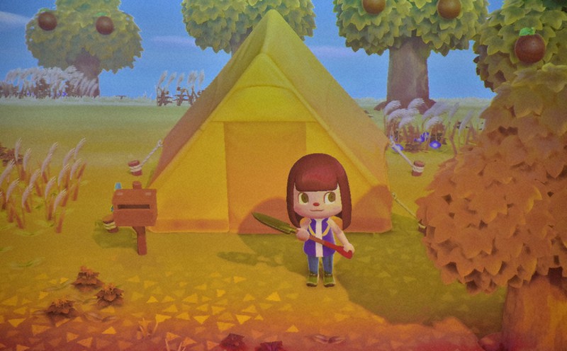 ゲームの中で「たんなん島」にある黄色いテント「たんなん島支所」の前で鉄のスコップを持つ丹南ともみさん2020年11月4日午前10時30分、横見知佳撮影