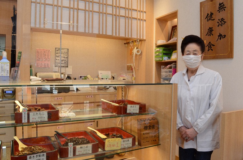 本店の店頭で2代目の水谷秀子さん。後ろに掲げられた「無添加健康食」は創業以来の誇りだ=東京都江東区の「佃宝 深川東雲本店」で11月11日午前、近藤浩之撮影