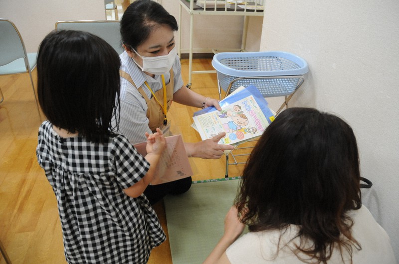 パンフレットを手に、ひざをついて健診を終えた母親に子育ての悩みを尋ねる保健師(中央)=東京都江戸川区のなぎさ健康サポートセンターで2020年8月27日午後1時34分、谷本仁美撮影