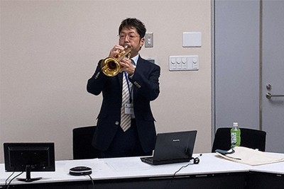 オンラインでは正確な音色や音域の表現が難しいことを体感してもらうためトランペットを吹く神代教授