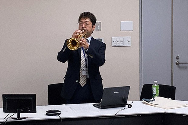 オンラインでは正確な音色や音域の表現が難しいことを体感してもらうためトランペットを吹く神代教授