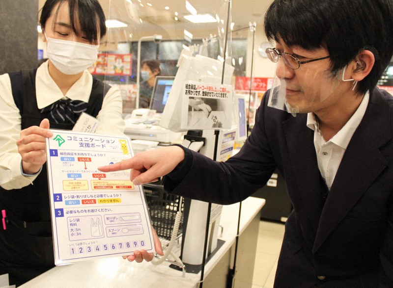 コープこうべ仁川店のレジでコミュニケーション支援ボードを使う志方龍さん(右)=宝塚市で 2020年11月30日午後6時25分、木田智佳子撮影