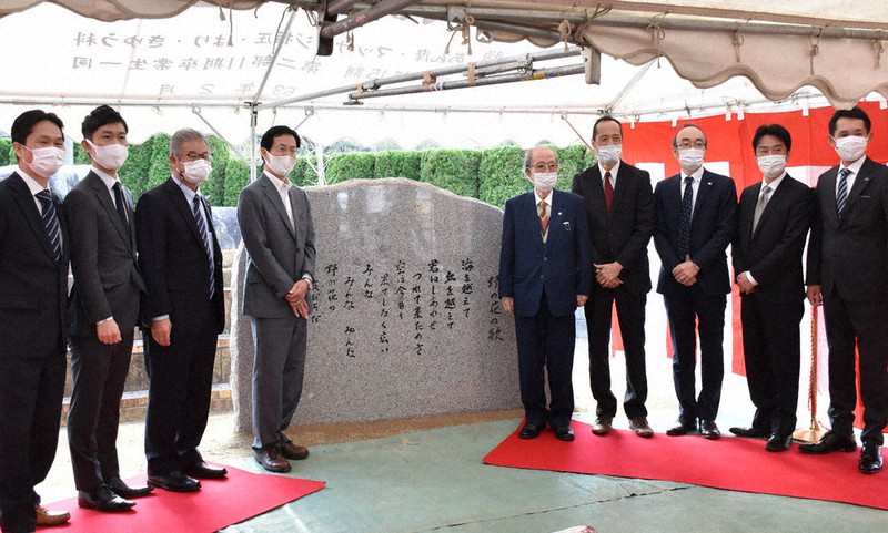 野の花の歌が刻まれた石碑と並んで記念撮影する福田理事長(中央右)ら