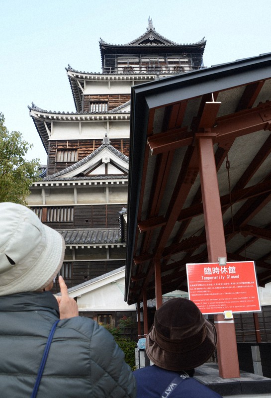 広島城前に設けられた臨時休館を知らせる看板を見つめる観光客=広島市中区で2020年12月12日午前10時32分、池田一生撮影