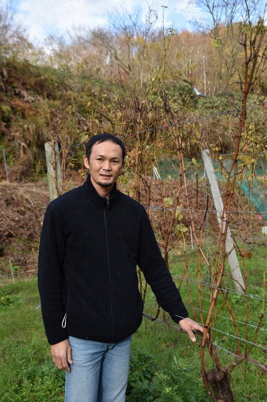 収穫を終えたブドウの木のそばに立つ田向俊さん=富山県氷見市余川のセイズファームで2020年12月3日午後2時30分、高良駿輔撮影
