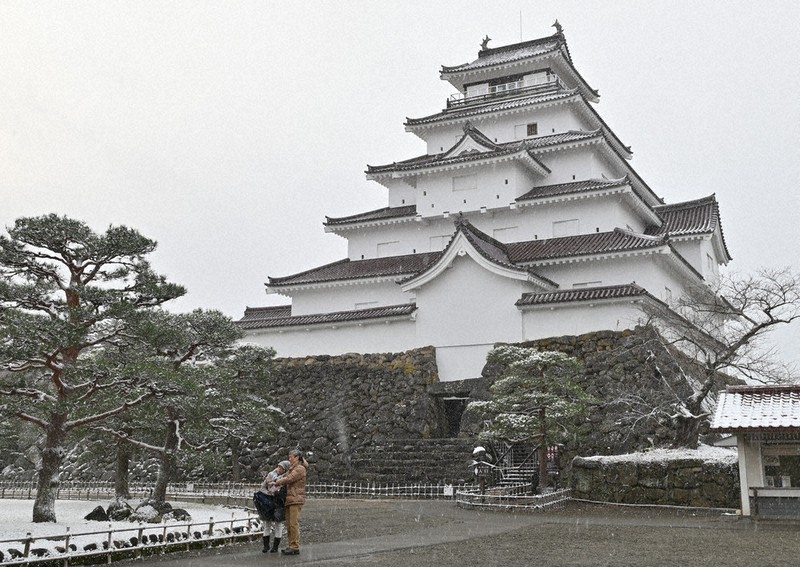 雪が積もった鶴ケ城天守閣を背景に写真撮影をする観光客=福島県会津若松市追手町で2020年12月15日、三浦研吾撮影