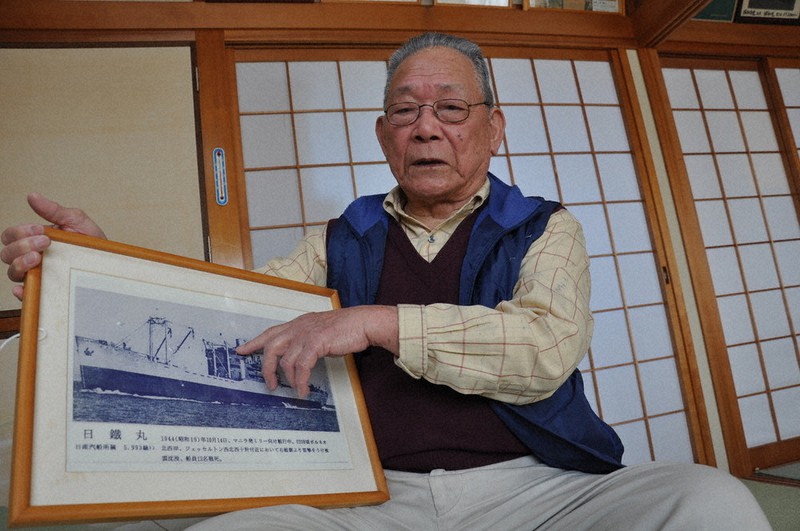 日鉄丸の写真を手に、米軍の攻撃を受けて沈没した状況を語る前田俊文さん。当時はまだ14歳の信号士だった=三重県志摩市で3月