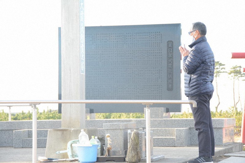 慰霊碑と慰霊塔の前で手を合わせる大学敏彦さん=仙台市若林区荒浜で11日