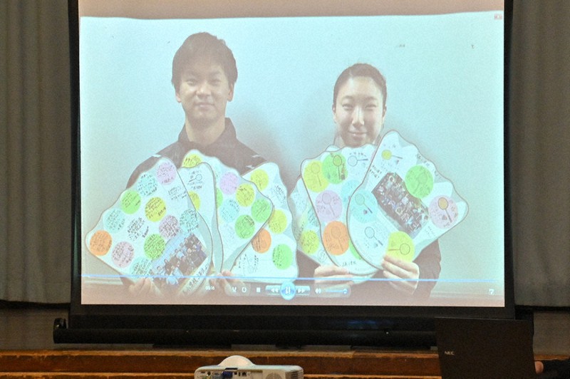 児童から送られた色紙を手に、お礼の言葉を伝える東野有紗選手(右)と渡辺勇大選手の動画も上映された=福島県猪苗代町立翁島小で2020年12月23日、三浦研吾撮影