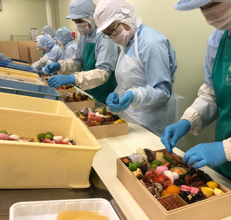 ベルトコンベアーを流れるお重におせち料理を盛り付ける従業員たち=八尾市の食品工場で2020年12月29日午前7時38分、隈元悠太撮影