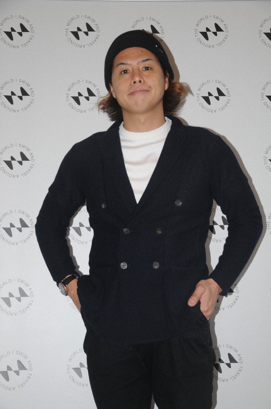 波をイメージしたブランドのロゴの前に立つYASUこと平井康翔さん=東京都内で2020年12月8日午後3時46分、田原和宏撮影