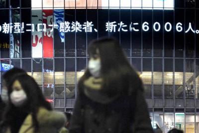国内感染者数が6000人を超えたことを伝えるニュースが流れる中、東京・渋谷駅前を歩く人たち＝2021年1月6日午後9時21分、竹内紀臣撮影