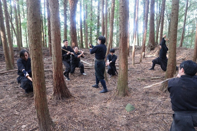忍者の衣装に身を包み、三重県伊賀市の山中で刀の使い方を学ぶ受講生たち=山田教授提供