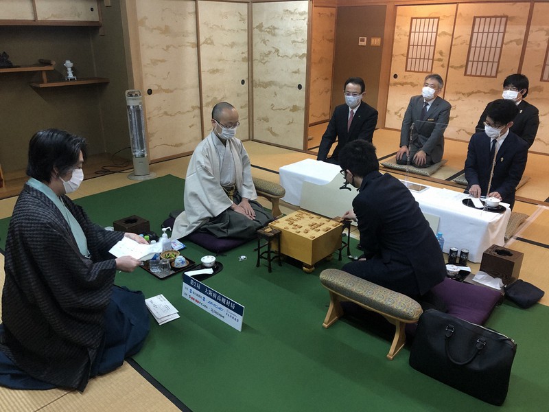 永瀬拓矢王座(後ろ姿)の封じ手を読み上げる立会の久保利明九段(左)。中央は渡辺明王将=大阪府高槻市で2021年1月24日午前8時59分、新土居仁昌撮影