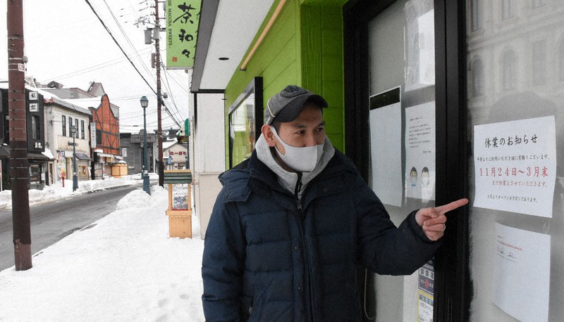 小樽堺町通り商店街で休業中の店の貼り紙を指さす坂口武さん。「11月24日~3月末まで休業」と記されている=北海道小樽市で1月29日、高橋由衣撮影