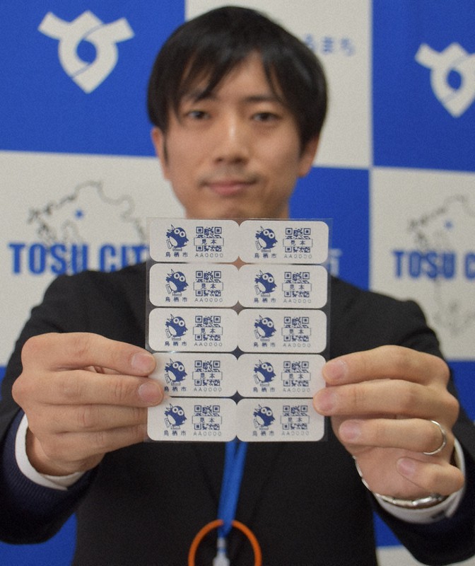「高齢者見守りシール」の見本を見せる鳥栖市職員