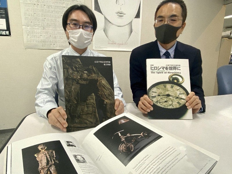 完成した図録を手に取る原爆資料館の落葉裕信学芸員(左)と旧図録を手にする加藤秀一副館長=広島市中区で2021年2月1日午前11時12分、賀有勇撮影