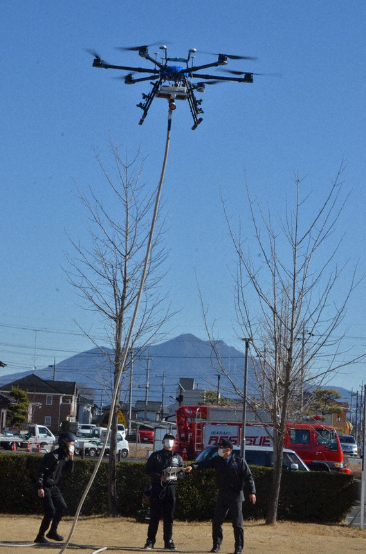 散水用ホースを付けて実演飛行する大型ドローン(背景は筑波山)=茨城県下妻市で2021年2月5日、安味伸一撮影