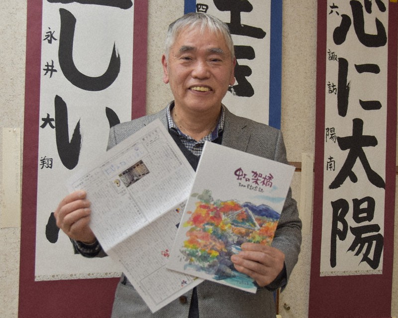 地域情報紙「虹の架橋」の300号記念誌(右)を手に笑顔を見せる松崎靖さん=群馬県みどり市大間々町大間々で2020年1月25日、大澤孝二撮影
