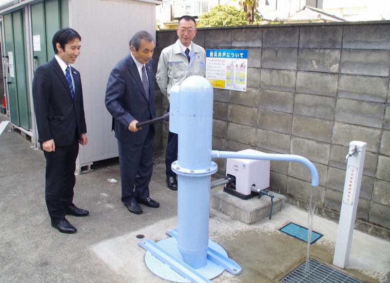地下30メートルから水をくみ上げる「日さく」の防災用手押し井戸を動かす若林直樹社長(中央)ら=さいたま市大宮区で2021年2月10日、山越峰一郎撮影