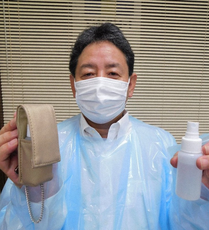 日本赤十字社に無償で送る医療用ガウンを着て、返礼品のケース付き消毒液スプレーを手にクラウドファンディングへの協力を呼び掛ける服部清隆社長=兵庫県豊岡市内で2021年3月2日午後6時24分、村瀬達男撮影