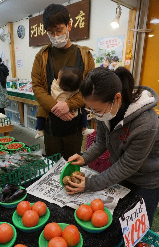 地元の八百屋でビニール包装されていない里芋を買い、新聞にくるんでもらう斎藤幸平さん(左)=大阪市で、清水有香撮影