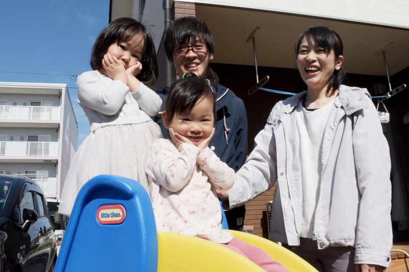自宅の庭で笑顔を見せる山根光保子さん(右)と夫辰洋さん(中央後ろ)。ポーズを取るのは長女さよりちゃん(左)と次女寧月ちゃん=福島県いわき市勿来町で2021年3月6日午前10時11分、渡部直樹撮影