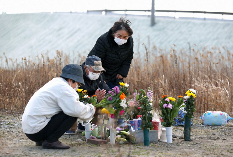 請戸郵便局で勤務中に津波に流され今も行方不明の長男健一さん(当時41歳)を悼み、跡地に作った献花台に花を供える佐藤一夫さん(中央)と妻のトシ子さん(右)。かさ上げ工事で県から献花台の撤去を要請されている。一夫さんは「ここで3月に花を供えるのは最後になるかもしれない」と話す=福島県浪江町で2021年3月10日、宮武祐希撮影