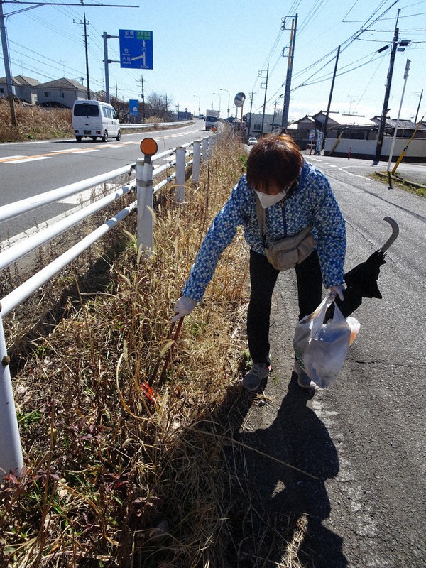道路脇の草むらに捨てられたごみを拾う神力富子さん=千葉県松戸市で2021年2月18日、小林多美子撮影