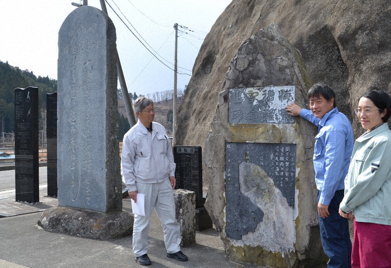 震災で破損し修復が完了した明治三陸大津波記念碑(右側)の前に立つ(左から)本郷町内会長の小池直太郎さんと日高真吾・国立民族学博物館教授ら=岩手県釜石市唐丹町で2021年3月16日午後1時54分、中尾卓英撮影