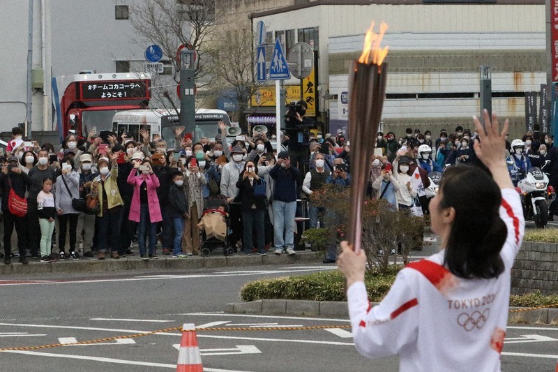 密集した状態で聖火ランナーにカメラを向けたり、手を振ったりするマスク姿の観衆=群馬県館林市の館林駅前で30日午前9時12分、妹尾直道撮影