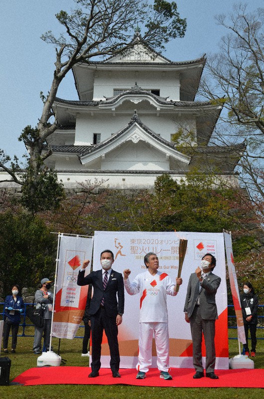 伊賀上野城前であった出発式で、トーチの炎を見上げる2021年4月8日の最初の聖火ランナーになった三重県出身の歌手、鳥羽一郎さん(68)=中央=と岡本栄市長(右)。左は鈴木英敬知事=三重県伊賀市上野丸之内で、大西康裕撮影