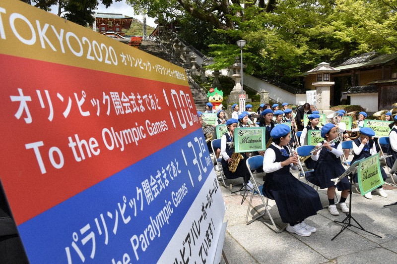 防府天満宮に設置された東京五輪開幕100日前を知らせるボードのそばで記念演奏する児童ら