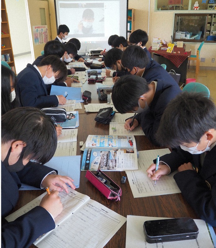 大型スクリーン(正面奥)越しに聞いた話を熱心にメモする生徒=兵庫県朝来市の和田山高で、松田学撮影