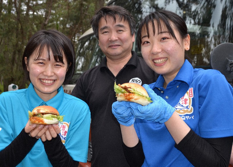 唐津市の虹の松原で「唐津Qサババーガー」を販売する(右から)永野悠希さん、吉田研一社長、山崎瑞季さん=佐賀県唐津市で2021年5月1日、峰下喜之撮影