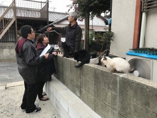 死亡した60代半ばの独居男性宅の隣に住み、残された猫の世話をすることになった男性（右）と話す福岡県古賀市環境課の職員＝同市提供