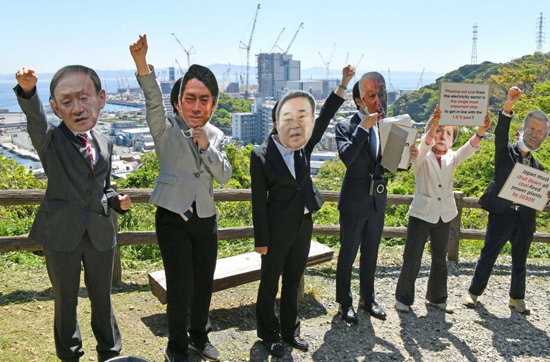 気候変動サミットに参加する政治家らにふんして石炭火力発電所建設反対を訴える人たち。奥は建設中の発電所=神奈川県横須賀市で2021年4月22日午前10時33分、丸山博撮影