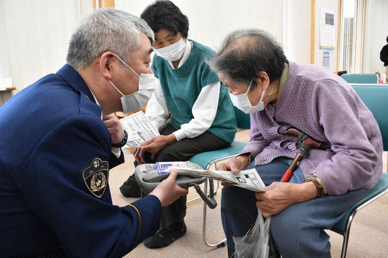 須坂署員(左)から特殊詐欺対策の説明を受ける高齢者(右)と付き添いの家族(奥)=長野県高山村牧の高山村保健福祉総合センターで2021年5月10日午後2時45分、皆川真仁撮影