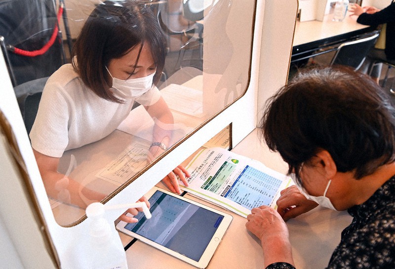 ワクチン接種予約支援窓口で、希望する日程や自宅近くの医療機関について高齢者から聞き取ってタブレットに入力する係員(左)=福岡県久留米市役所で10日、徳野仁子撮影