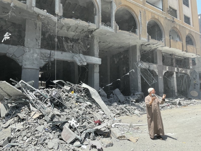 イスラエル軍の攻撃で破壊されたビルの前に立ち尽くす近隣住民=パレスチナ自治区ガザ地区ガザ市で2021年5月12日午後1時34分、三木幸治撮影