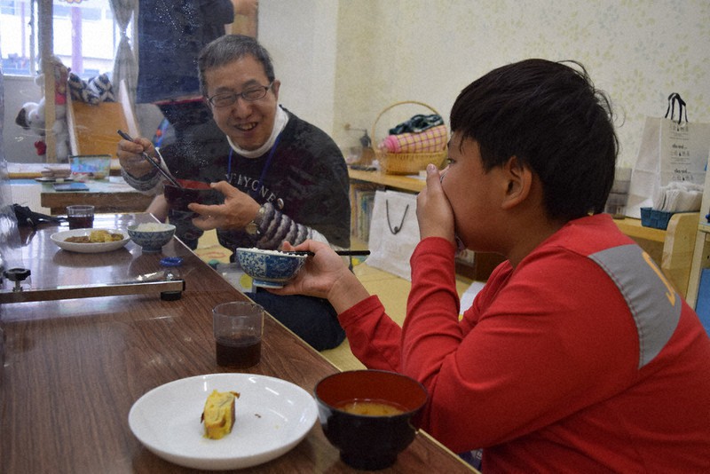 ビニールシート越しに子どもたちと食事して笑顔を見せる原田さん(奥)=北九州市八幡東区で、青木絵美撮影