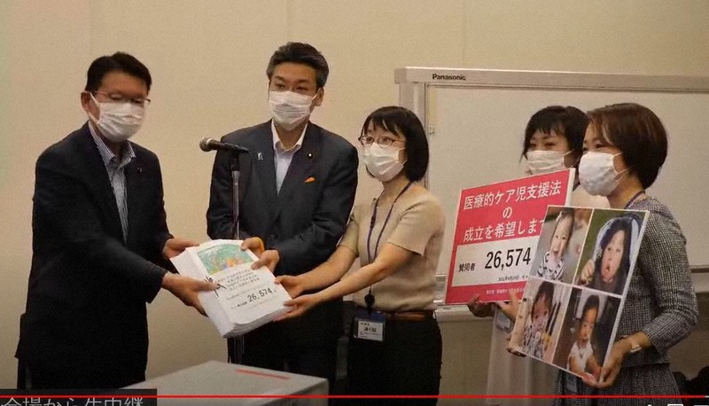 衆院厚生労働委員会の与野党筆頭理事に、法の早期成立を求める署名を手渡す医療的ケア児の保護者ら=14日午後、東京・永田町の議員会館からの生中継画面から