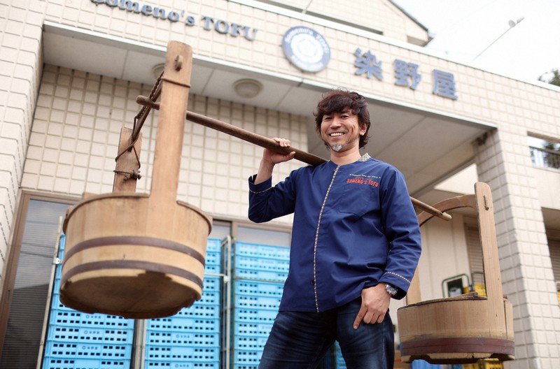 かつて豆腐の販売で使われていたおけを肩に乗せ、ポーズをとる染野屋の小野篤人社長=茨城県取手市で、小川昌宏撮影