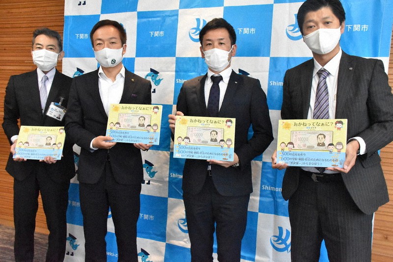 絵本「おかねってなぁに?」を掲げる高山会長(左から3人目)と前田市長(同2人目)