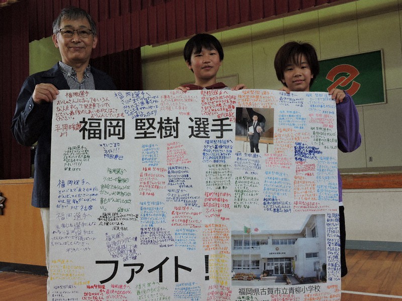 福岡選手への応援メッセージを手にする父親の綱二郎さん(左)と青柳小の児童