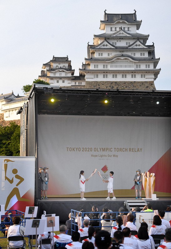 新型コロナウイルスの影響で公道での開催が中止となり、姫路城の広場に設置されたステージ上でトーチキスをする聖火ランナーたち=兵庫県姫路市で2021年5月23日午後5時57分、滝川大貴撮影