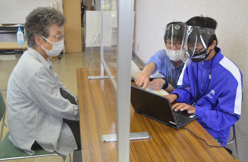 予約業務を手伝う中学生(右)=千葉県睦沢町役場で